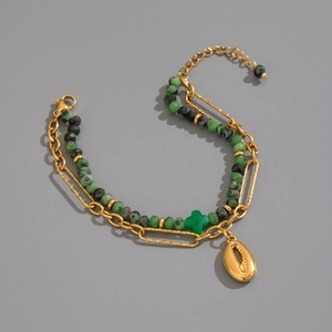 Detailed view of double-layer beaded bracelet with green cross and golden shell charms