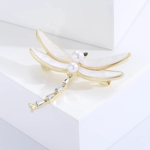 Macro detail of a dragonfly brooch with shell wings and white pearls on a display