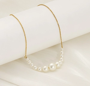 Close-up of white pearls in gradient sizes on a gold chain over soft white silk fabric