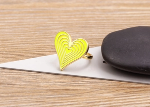 Detailed view of yellow heart enamel ring with layered concentric shapes on wood background