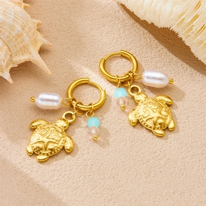 Gold-plated turtle earrings with white pearls and blue beads on a sandy beach setting