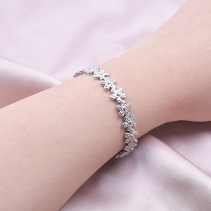 Close-up of silver floral chain bracelet with matte petals worn on wrist over pink silk