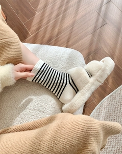 Close-up of black and white striped wool socks with thick plush slippers on wooden floor
