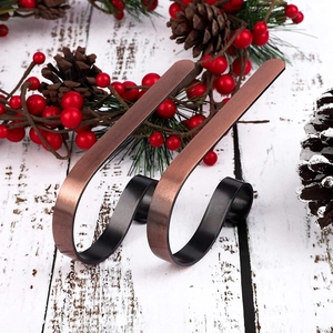 Detail of S-shaped metal Christmas stocking hooks on a white wood surface with holiday decor