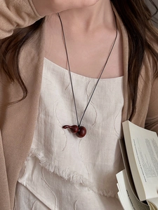 Détail d'un collier avec pendentif en bois de gourde porté sur une tenue minimaliste