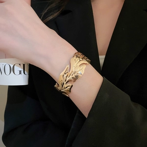Detailed view of wide gold leaf-shaped cuff bracelet with polished metallic finish