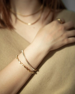 Detail of layered gold box chain bracelets and matching jewelry on a model