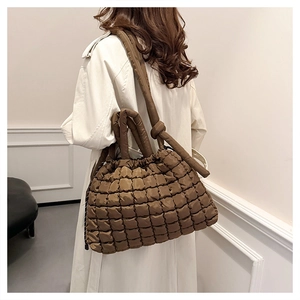 Detail of a brown quilted puffer tote bag with elegant knot handle worn by a model