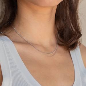 Close-up of double-layer silver beaded necklace and snake chain worn on model neck