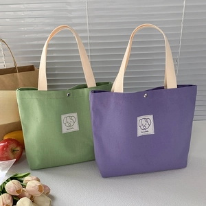 Detail of green and purple canvas tote bags with cute cartoon labels and silver snap buttons