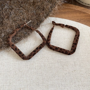 Détail de créoles carrées avec flocage léopard marron sur fond en lin beige