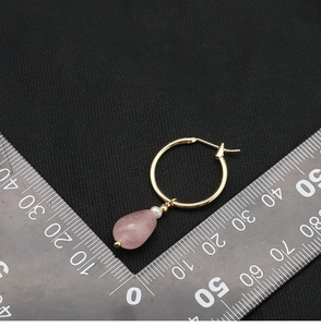 Macro shot of gold hoop earring with pink quartz and pearl pendant next to a ruler