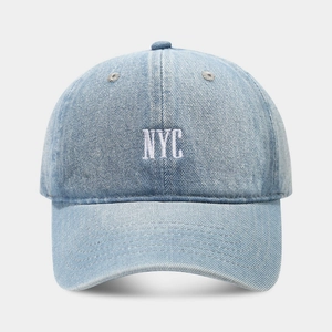 Detailed close-up of light blue denim baseball cap with white NYC embroidery and twill texture