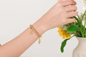 Detail of a golden beaded bracelet featuring Hamsa Hand pendants on a woman's wrist