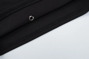 Close-up of black ribbed knit fabric detail with silver metal grommet and fine stitching