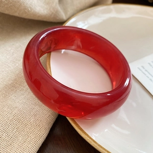 Detail view of a thick translucent red resin bangle placed on a white ceramic dish