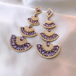Detail of tiered fan-shaped earrings with purple teardrop crystals and gold finish