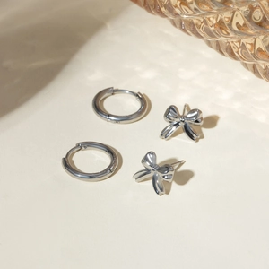 Close-up of minimalist silver stainless steel hoop earrings and delicate bow stud earrings