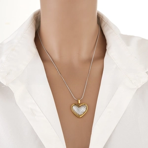 Detail of two-tone gold and silver heart pendant on a thin chain worn with white shirt