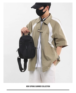 Close-up of a men's black oxford fabric crossbody chest bag held by hand in a studio