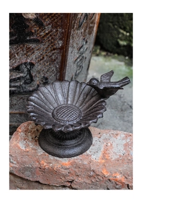 Detail of vintage cast iron sunflower bird feeder with bird figurine on brick
