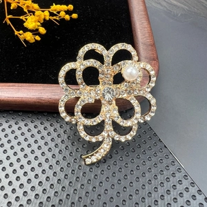 Macro detail of a vintage clover brooch featuring sparkling rhinestones and a white pearl