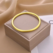 Close-up of a minimalist solid gold titanium steel bangle on a beige jewelry box