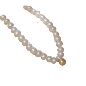 Elegant natural white pearl necklace with a minimalist gold ball pendant on white background