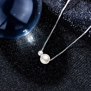 Macro shot of double white faux pearl pendant with a fine silver box chain on black