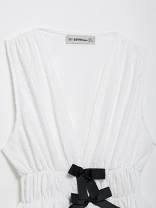 Détail du haut blanc sans manches avec col en V, texture plissée et ruban de ceinture noir