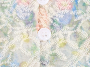 Détail de la broderie blanche sur tissu floral transparent avec un bouton rond
