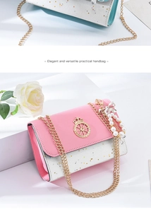 Detail of pink and white crossbody bag with gold crown emblem and pearl chain accessory