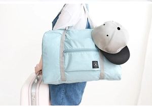 Model wearing a light blue foldable travel bag on shoulder with luggage and a cap