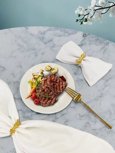 Macro detail of golden tiger shaped metal napkin rings on white linens with marble background