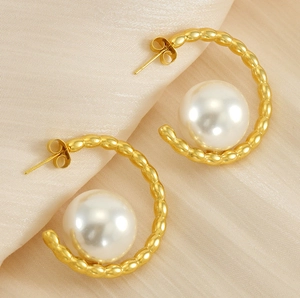 Detail of C-shaped golden pearl earring on champagne silk background with beaded texture