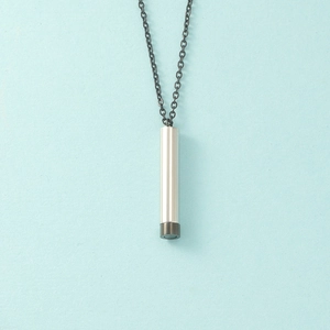 Close-up of a silver cylindrical pendant with black base on a dark metal chain