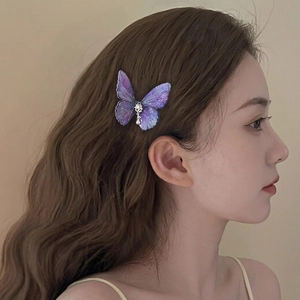 Elegant purple butterfly hair clip with shimmering gold details and pearl accent on wavy hair