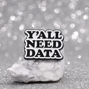 Macro shot of 'Y'ALL NEED DATA' enamel pin badge on a white decorative stone base