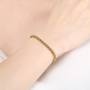 Detail of a golden wheat chain bracelet showing the woven texture on a model wrist