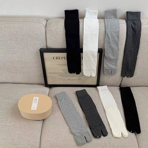Close-up of ribbed Tabi socks in black, white, and grey displayed on a sofa