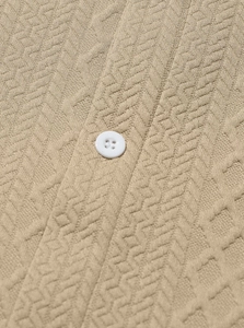 Macro shot of beige knit fabric texture with herringbone pattern and white resin button