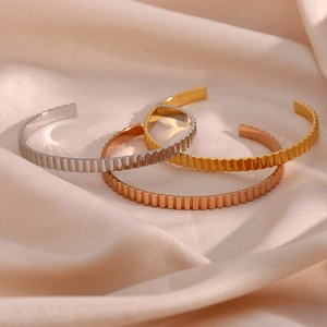 Close-up of three-color minimalist vertical ribbed stainless steel open bangles on silk