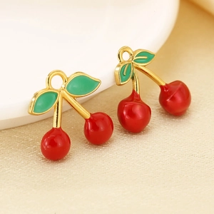 Close-up of enamel cherry charms with red fruit and green leaves on a ceramic plate