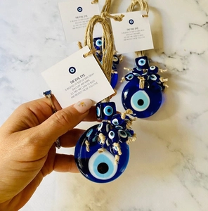 Hand holding Evil Eye glass pendant with rope cord and blessing card against marble background