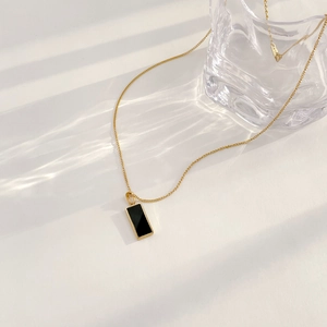 Detail of 18K gold necklace with black onyx square pendant under artistic light shadows
