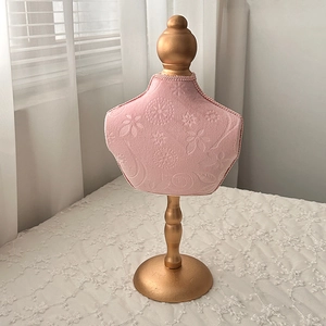 Detail of pink velvet jewelry bust stand with floral embossing and gold metal base