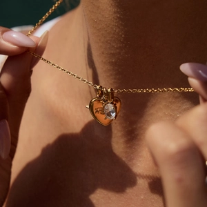 Close-up of a gold heart necklace with a clear gemstone and 'my' engraving on fine chain