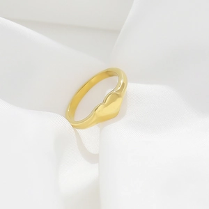 Macro detail of a golden heart-shaped minimalist ring resting on elegant white silk fabric