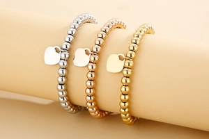 Three beaded bracelets in gold silver and rose gold with heart tags on a display