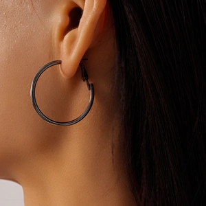Close-up of black metallic geometric hoop earrings worn with sleek polished finish